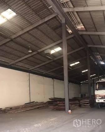 Warehouse for rent in Chachoengsao - Interior aisle showing steel columns, stacked materials and ample storage space beneath the roof.