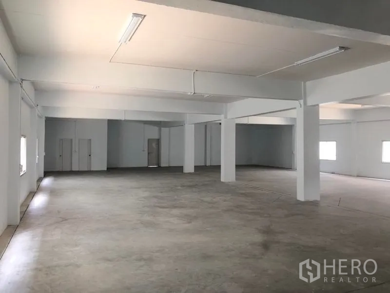 Factory for rent in Pak Kret, Nonthaburi - Spacious warehouse hall with concrete floor, columns and fluorescent lighting.