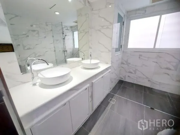 Condominium for rent in Watthana, Bangkok - Modern bathroom with double vessel sinks, large mirror and glass shower with marble-effect tiles.