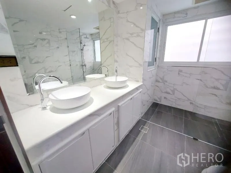 Condominium for rent in Watthana, Bangkok - Modern bathroom with double vessel sinks, large mirror and glass shower with marble-effect tiles.
