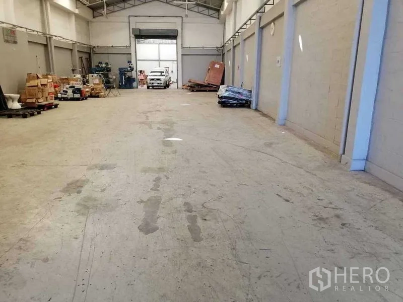 Warehouse for rent in Samut Prakan - Spacious high-ceiling storage hall with concrete floor and a large rear roller door.