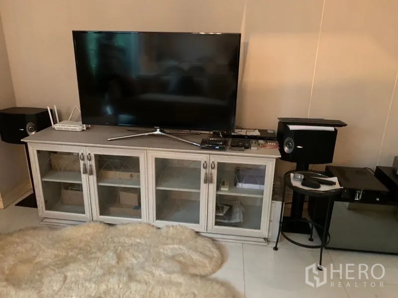 Townhouse for sale in Watthana, Bangkok - Living room media wall with large flat-screen TV, speakers and glass-door cabinet.