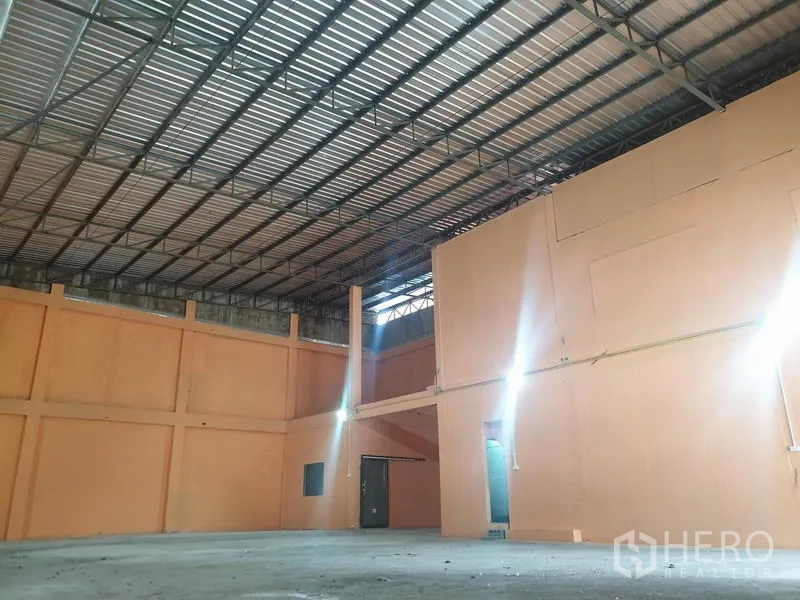 Warehouse for rent in Din Daeng, Bangkok - Open-plan storage area featuring steel roof structure, mezzanine wall and bright industrial lighting.
