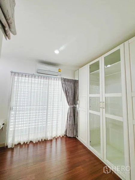 Townhouse for rent in Phra Khanong, Bangkok - Compact bedroom with glass-front wardrobes and balcony doors.