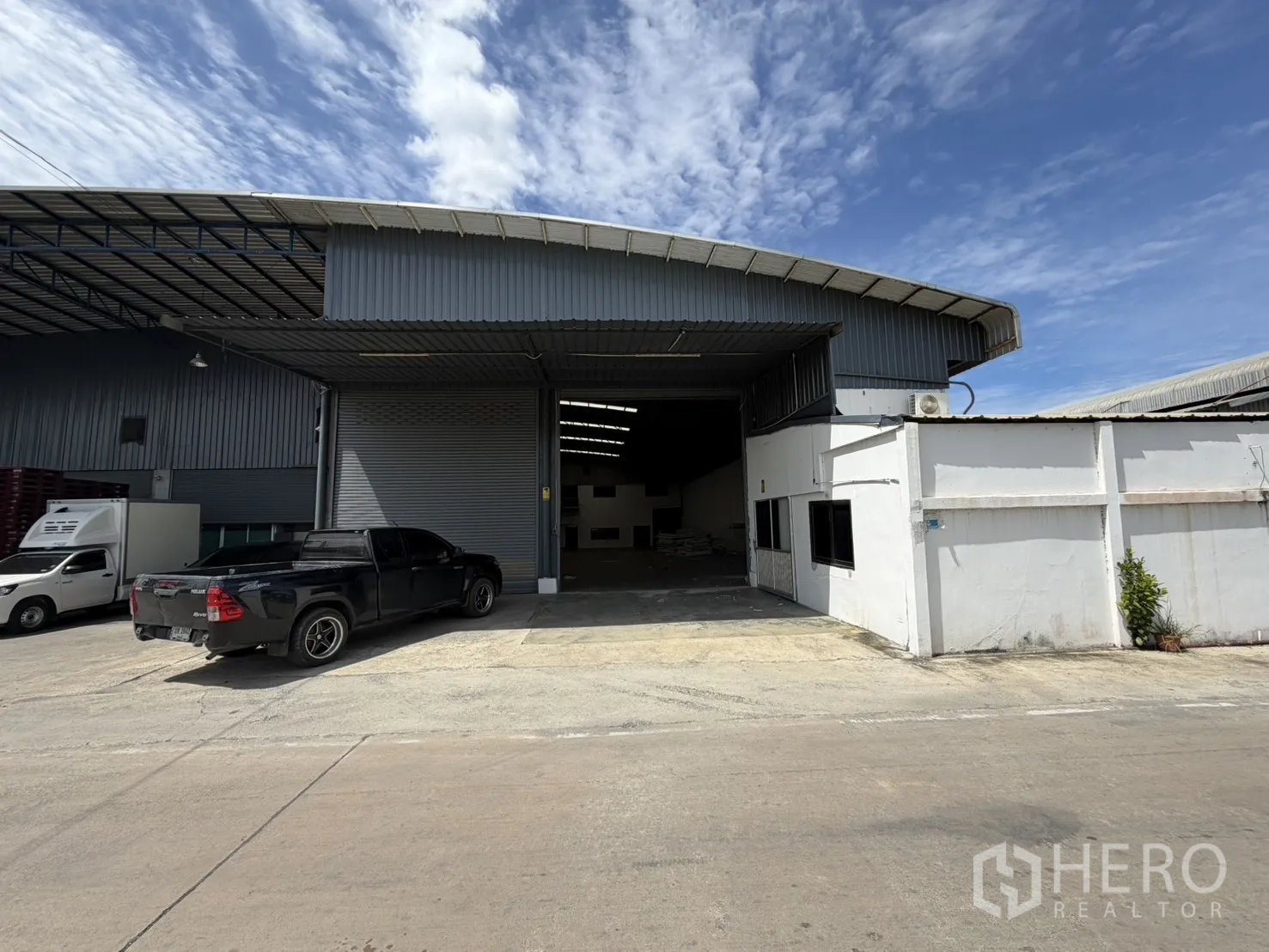 Warehouse for rent in Khlong Luang, Pathum Thani - Warehouse exterior with covered loading bay, wide roller shutter door, and paved forecourt for vehicle access.