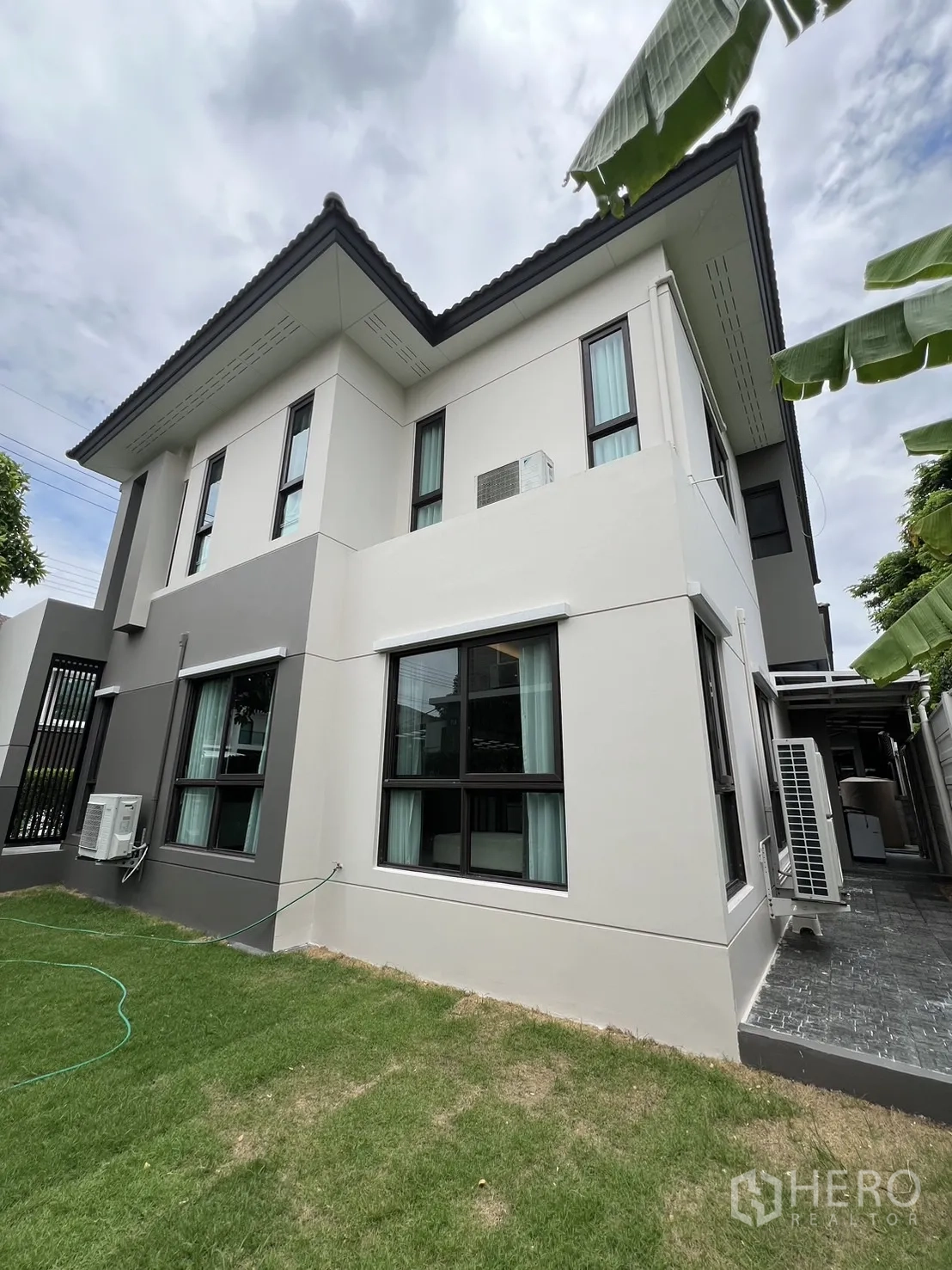 Detached House for rent or sale in Prawet, Bangkok - Side exterior of the house with lawn and black-framed windows.