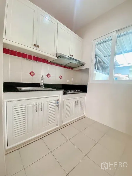 Townhouse for rent in Prawet, Bangkok - Fitted kitchen with white cabinets, cooktop, hood and black granite countertop.