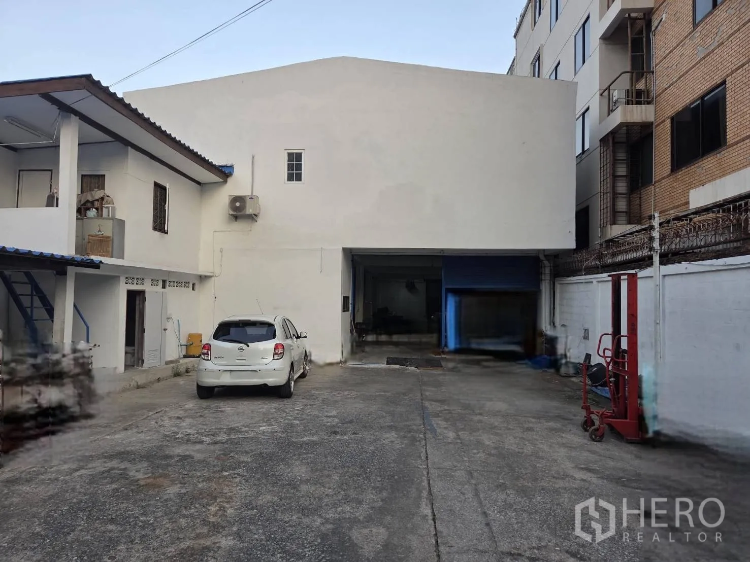 Warehouse for rent in Ratchathewi, Bangkok - Walled warehouse exterior with private forecourt, parking space, and a large roll-up loading door beside a small office annex.