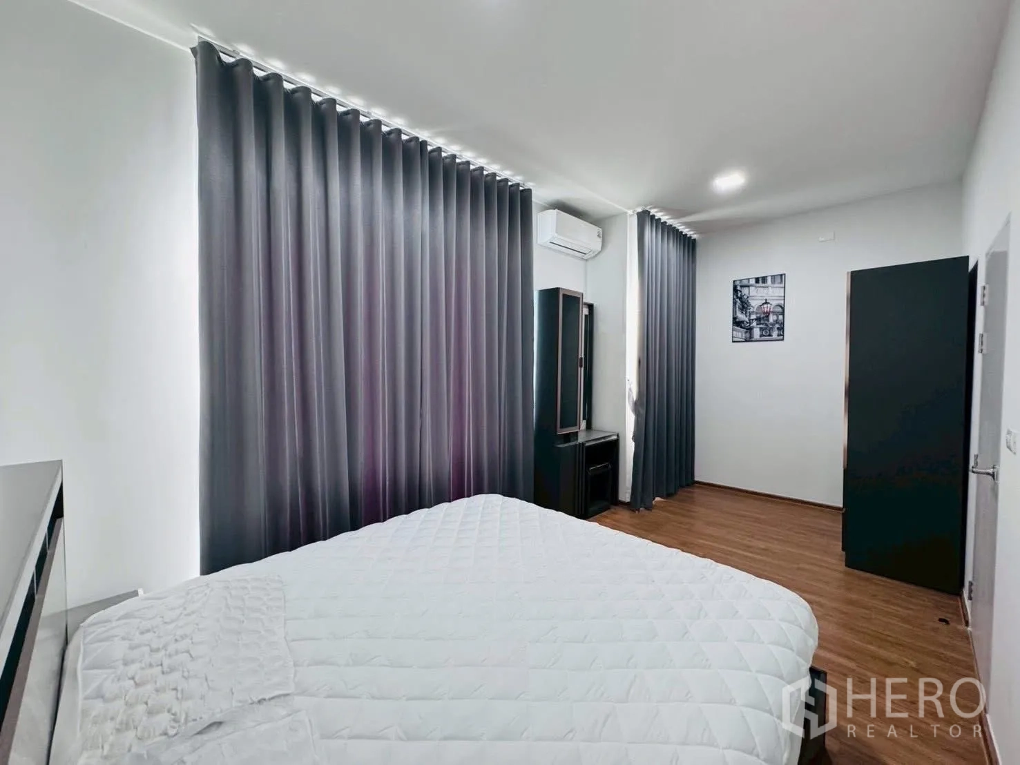 Townhouse for rent in Bang Phli, Samut Prakan - Spacious master bedroom with large bed, vanity, grey curtains and warm wood flooring.
