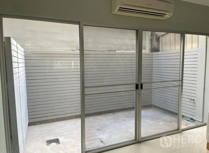 Townhouse for rent in Suan Luang, Bangkok - Enclosed outdoor courtyard viewed through floor-to-ceiling sliding glass doors with insect screens.