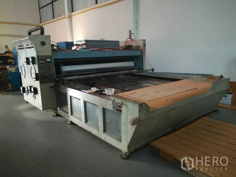 Factory for sale in Bang Len, Nakhon Pathom - Large processing machine with feed table and cardboard on a concrete floor.