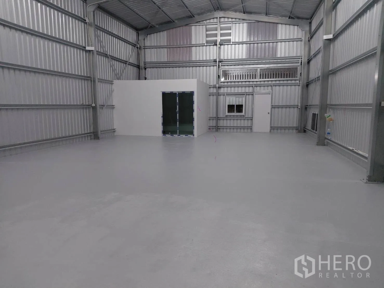 Warehouse for rent in Lat Phrao, Bangkok - Open steel-frame warehouse interior with high roof, smooth floor, and an enclosed office with glass door and window.