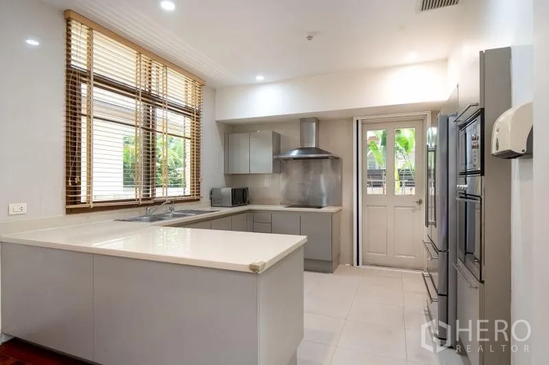 Detached House for rent in Watthana, Bangkok - Bright L-shaped kitchen with white countertops, stainless range hood and door to the garden.