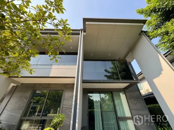Detached House for rent in Bang Kapi, Bangkok - Close-up of sleek upper facade with glass balcony and wide eaves among greenery.
