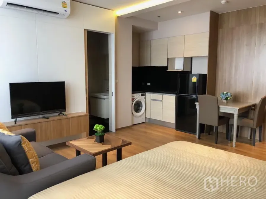 Condominium for rent in Khlong Toei, Bangkok - Modern studio condo interior with kitchenette, washing machine, TV and dining nook.