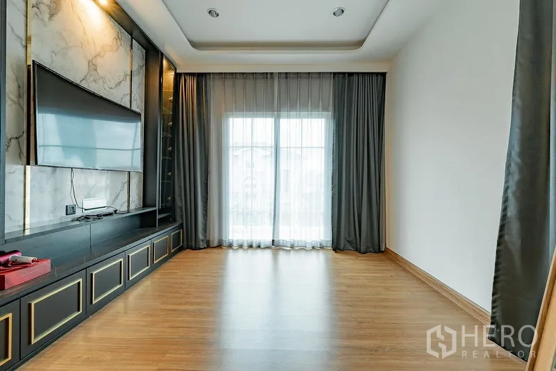 独立式住宅 出租或出售在Bang Khen, Bangkok - 宽敞房间，木地板、深色内置电视柜，推拉门通向阳台。