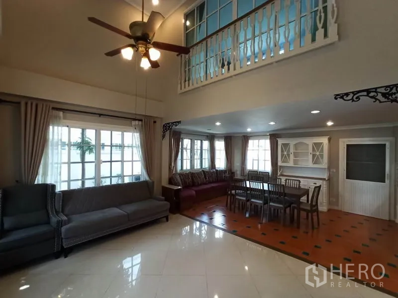 Detached House for rent in Mueang Samut Prakan, Samut Prakan - Double-height living room with ceiling fan, large windows, sofas and adjoining dining area with classic railing.