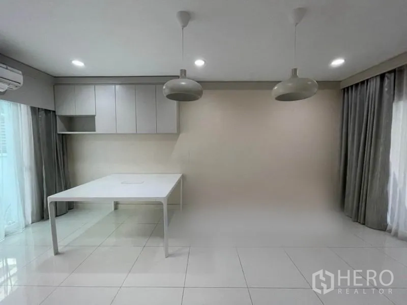 Townhouse for sale in Suan Luang, Bangkok - Dining space with large windows, white tile floors and overhead pendants beside built-in wall cabinets.