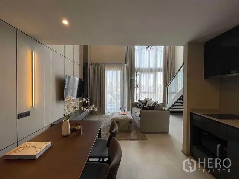 Condominium for rent in Pathum Wan, Bangkok - Open-plan dining toward the living room with floor-to-ceiling curtains, balcony access, staircase and TV feature wall.