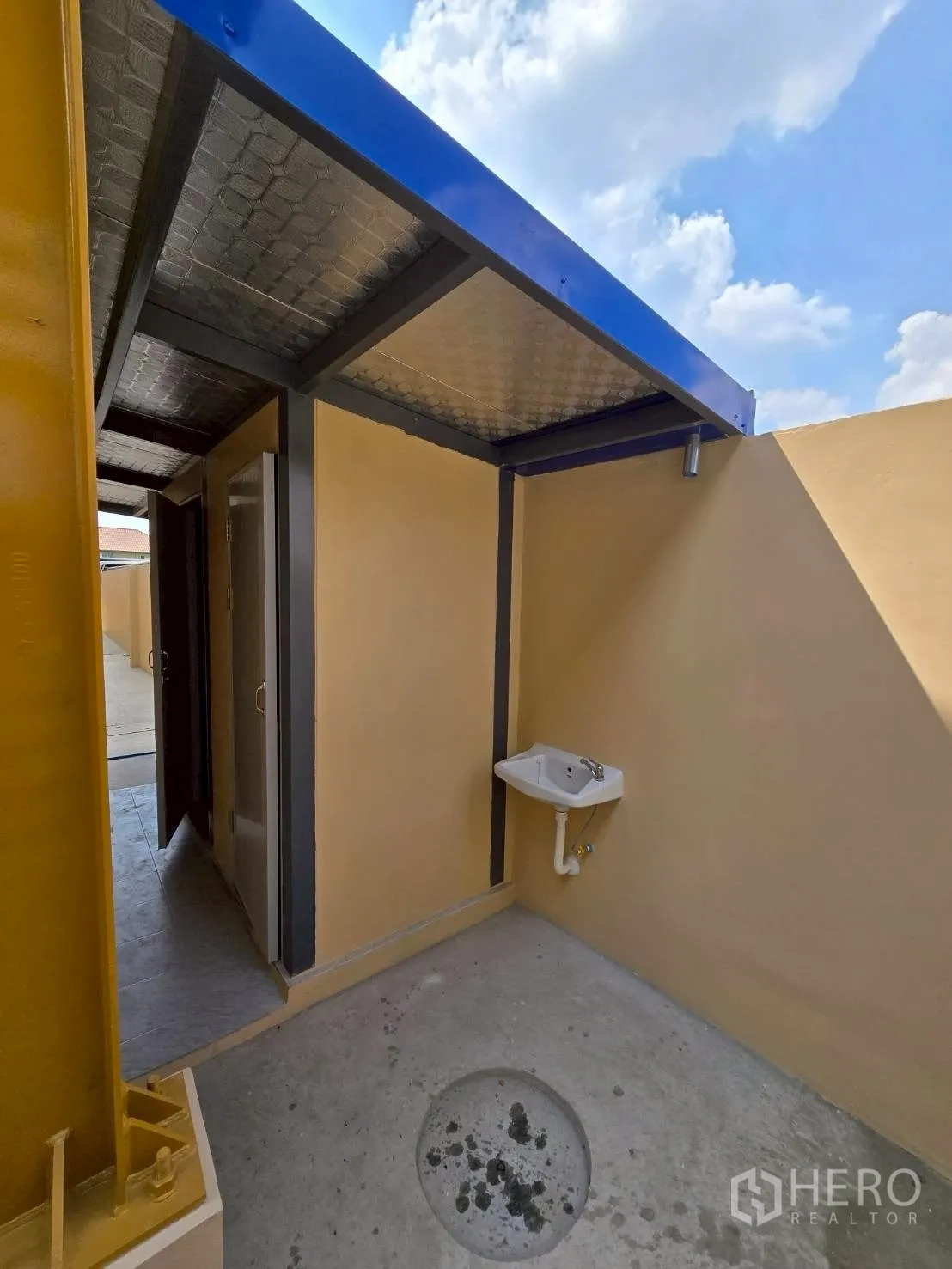Warehouse for rent in Khlong Sam Wa, Bangkok - Utility area with metal canopy, restroom doors, and wall-mounted sink beside a concrete floor in a warehouse.