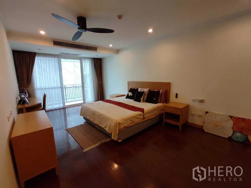 Condominium for rent in Khlong Toei, Bangkok - Spacious bedroom with large window, desk, wood flooring and soft lighting.