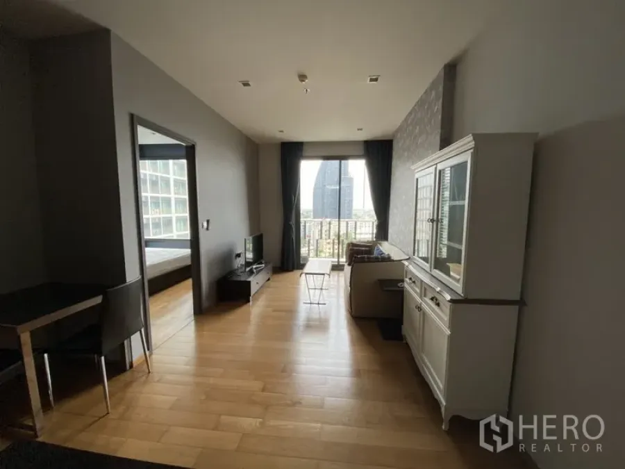 Condominium for rent in Khlong Toei, Bangkok - Bright living room with wood flooring, sofa, TV console and balcony doors opening to a city view