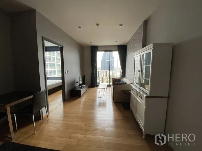 Condominium for rent in Khlong Toei, Bangkok - Bright living room with wood flooring, sofa, TV console and balcony doors opening to a city view