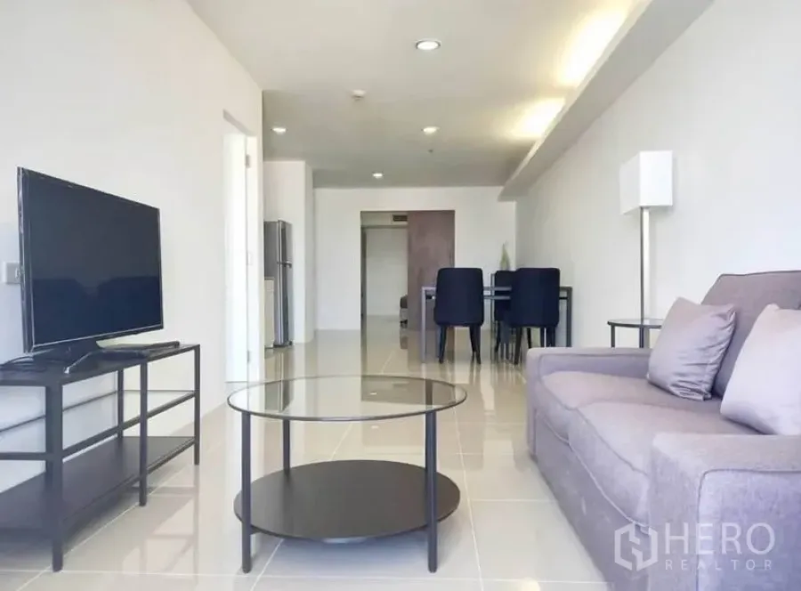 Condominium for rent in Khlong Toei, Bangkok - Bright open-plan living room with gray sofa, glass coffee table, TV stand and a dining area.