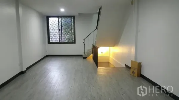 Shophouse for rent in Watthana, Bangkok - Open-plan ground floor with wood-look flooring, window grille and stairs to upper level.