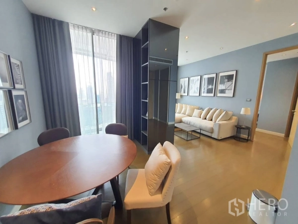 Condominium for rent in Pathum Wan, Bangkok - Open-plan dining area with round wooden table and upholstered chairs beside tall windows.