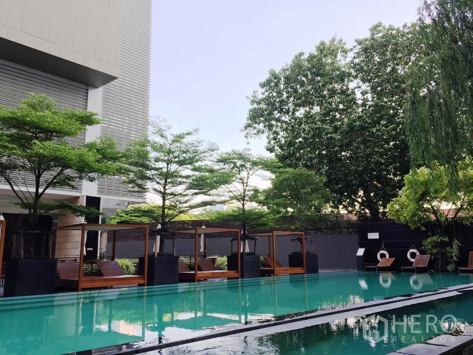 Condominium for rent or sale in Khlong Toei, Bangkok - Outdoor swimming pool with cabanas and landscaped trees.