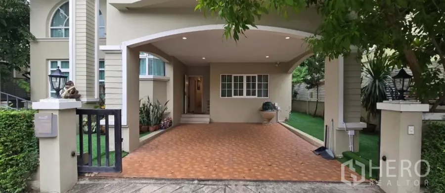 Detached House for rent in Mueang Pathum Thani, Pathum Thani - Covered carport and entryway of the detached house with tiled driveway and garden.