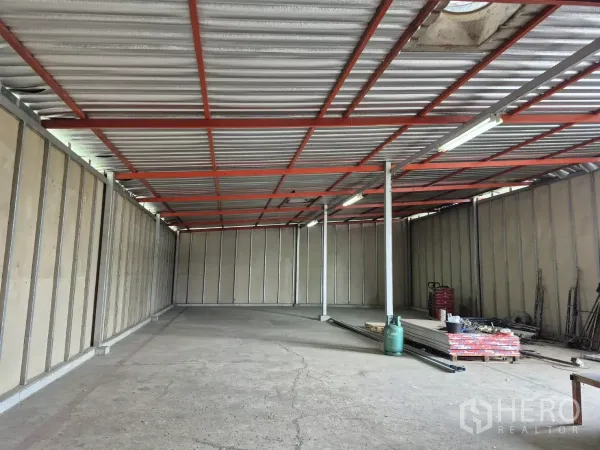 Warehouse for rent in Mueang Pathum Thani, Pathum Thani - Spacious storage hall with metal ceiling, support columns and materials stacked along the side walls.