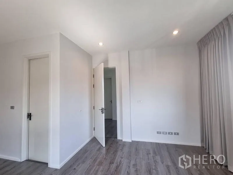 Detached House for rent - Minimalist bedroom corner with recessed lights, grey wood flooring and two white doors.