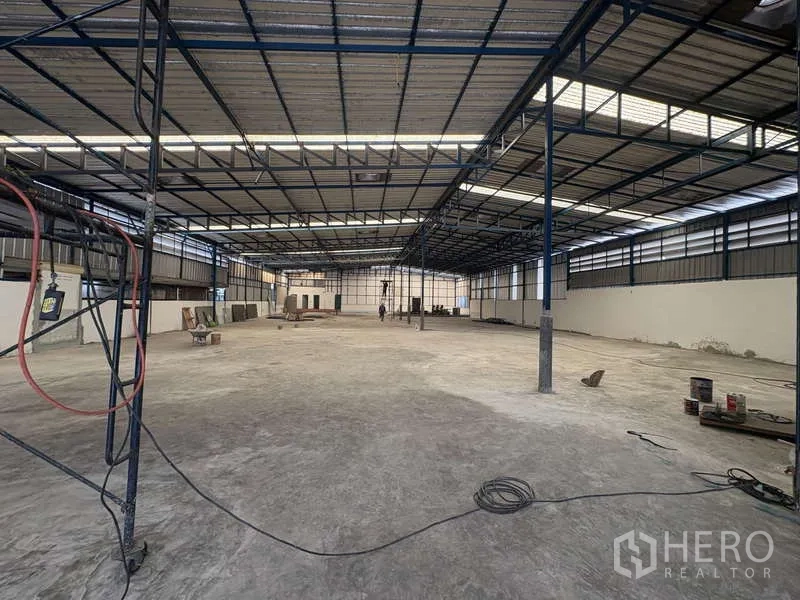 Warehouse for rent in Prawet, Bangkok - Spacious clear-span warehouse interior featuring a steel truss roof with skylight panels, ventilation windows, and a level concrete floor.