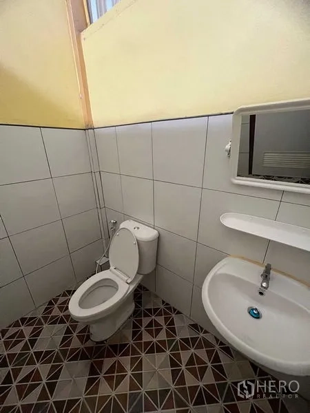 Warehouse for rent in Lat Krabang, Bangkok - Compact restroom with tiled walls and floor, a toilet, sink, and wall mirror.