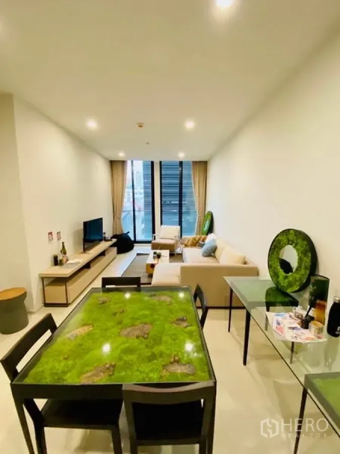 Condominium for rent in Pathum Wan, Bangkok - Bright open-plan living and dining room with floor-to-ceiling windows, TV console, and a glass table.