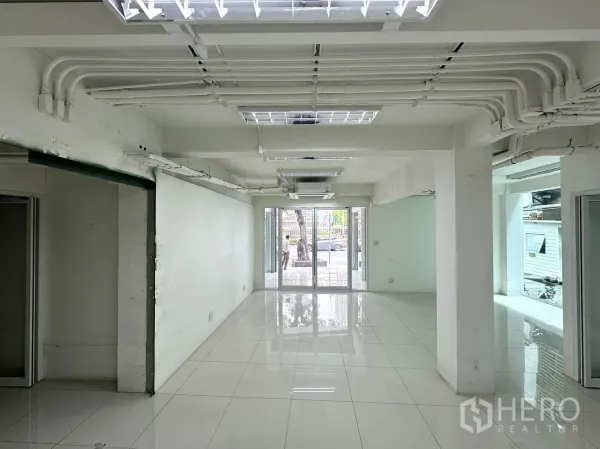 Retail Space for rent in Bang Rak, Bangkok - Long retail hall with exposed ceiling conduits and glass entrance doors facing the street.