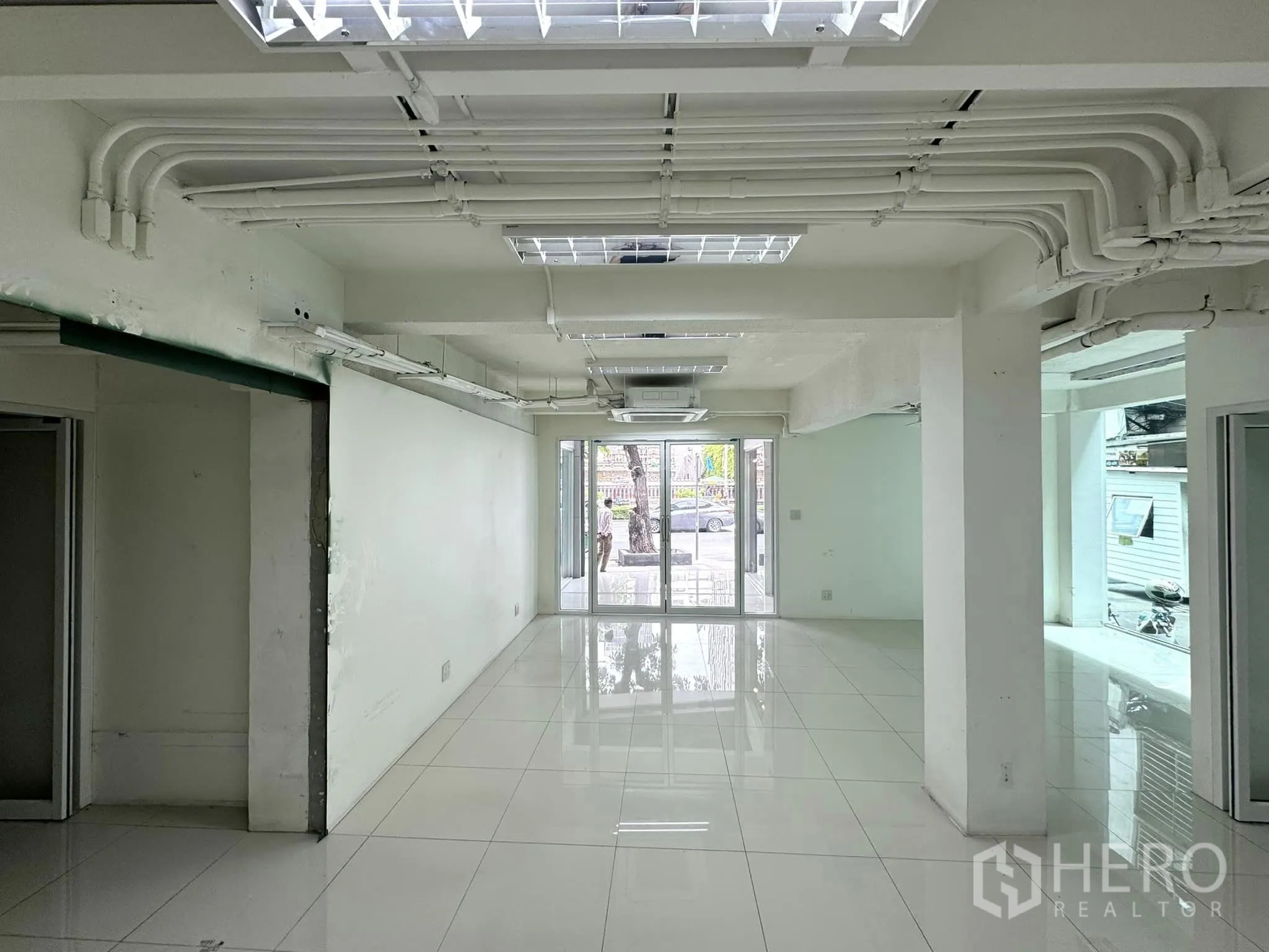 Retail Space for rent in Bang Rak, Bangkok - Long retail hall with exposed ceiling conduits and glass entrance doors facing the street.