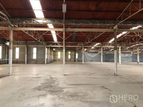 Factory for rent in Bang Phli, Samut Prakan - Large industrial interior showing column grid, roof skylights and corrugated wall panels around a spacious work area.