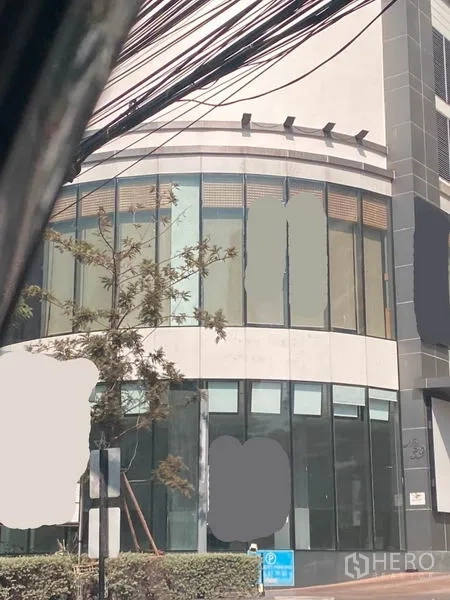 Retail Space for rent in Watthana, Bangkok - Close-up of ground-floor retail façade with tall glass panels, entry door, and landscaped sidewalk.