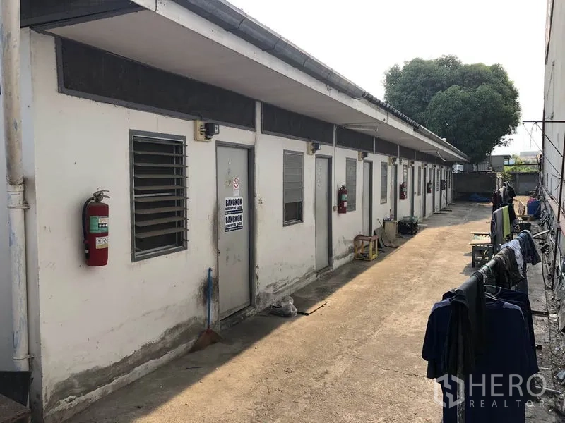 Factory for rent in Bang Bua Thong, Nonthaburi - Row of workers’ accommodation rooms with fire extinguishers along a narrow walkway.