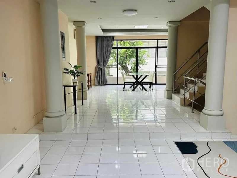 Home Office for rent - Light-filled living area with columns, staircase and dining nook by wide windows.