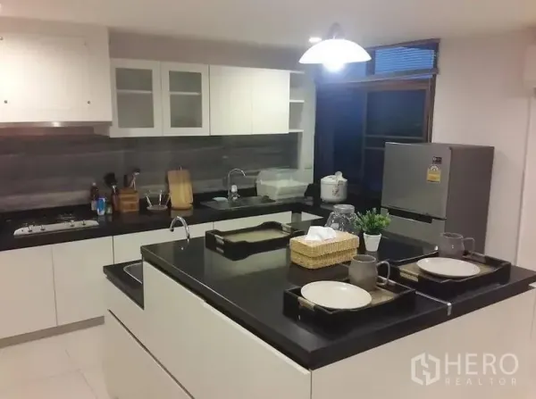 Townhouse for rent in Khlong Toei, Bangkok - Contemporary kitchen with white cabinetry, black granite island, pendant light, and stainless appliances.