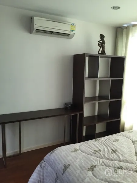Condominium for rent or sale in Khlong Toei, Bangkok - Bedroom corner with air-conditioner, open shelving unit and slim desk beside a window.