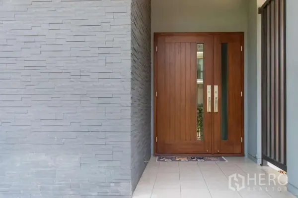 Detached House for rent or sale in Kanchanaburi - Close-up of solid wooden front door beside a gray stone feature wall at the entrance.