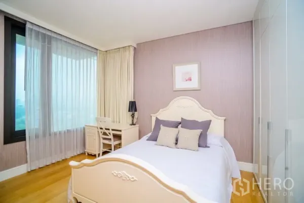 Condominium for rent in Khlong Toei, Bangkok - Light second bedroom with white bed, study desk by the window, sheer curtains and a wardrobe.