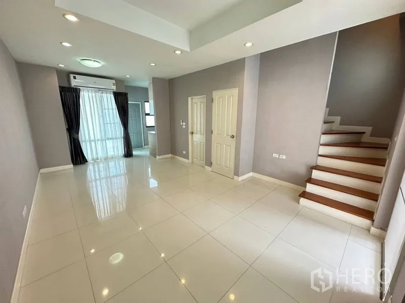 Townhouse for rent or sale in Phra Khanong, Bangkok - Ground-floor living and dining area with white tiles, recessed lights, and staircase.