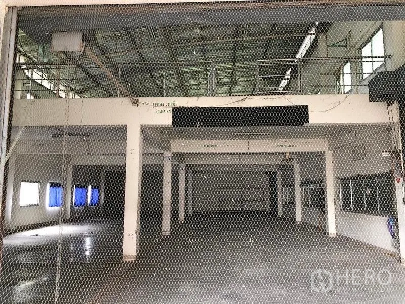 Factory for sale in Lam Luk Ka, Pathum Thani - Spacious manufacturing hall viewed through safety mesh with mezzanine level above.