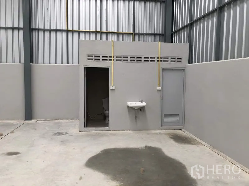 Warehouse for rent in Lat Krabang, Bangkok - On-site restroom block with sink inside the warehouse and exposed utility lines.